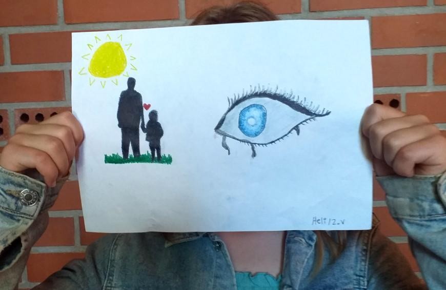 Tyttö pitelee kasvojensa edessä piirutusta, johon on piirtänyt ikävän vankilassa olvevaa isää kohtaan