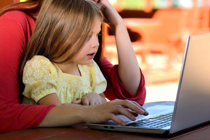 Pieni tyttö äidin sylissä tietokoneella